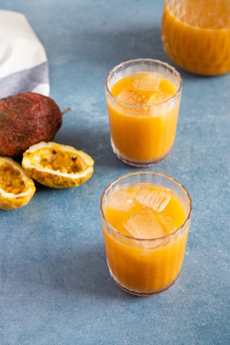 Two glasses of chilled passion fruit juice (jugo de chinola) with ice, served with fresh passion fruit on the side.