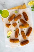 Golden tuna and potato croquettes served on parchment with creamy cilantro dipping sauce and a lemon wedge.