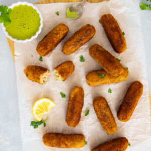 Golden tuna and potato croquettes served on parchment with creamy cilantro dipping sauce and a lemon wedge.