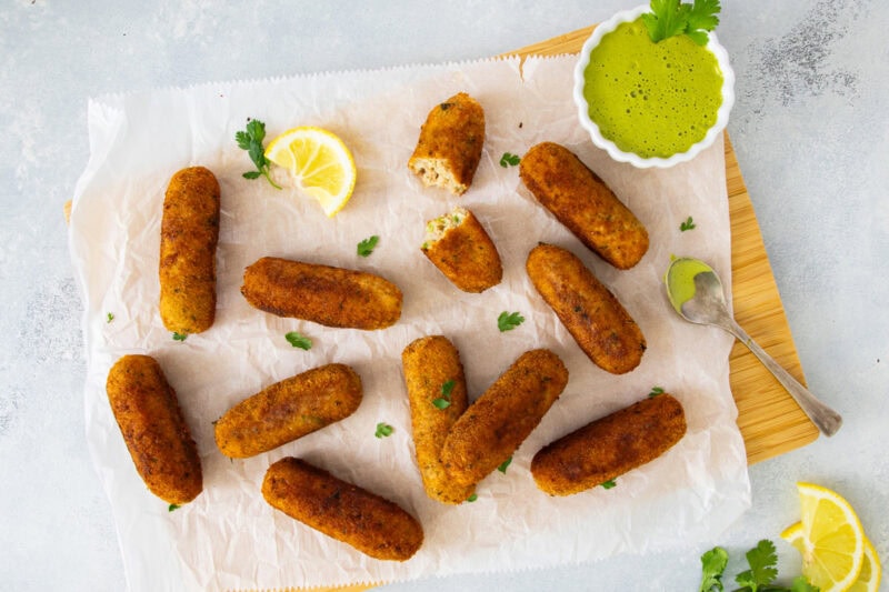 Golden tuna and potato croquettes served on parchment with creamy cilantro dipping sauce and a lemon wedge.