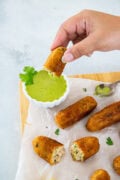 Golden tuna and potato croquettes served on parchment with creamy cilantro dipping sauce and a lemon wedge.