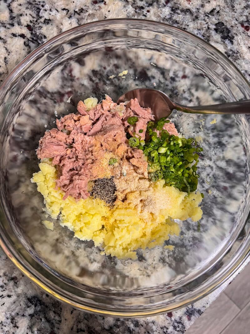 Mixing ingredients for croquettes: mashed potatoes, tuna, spices, and chopped herbs.