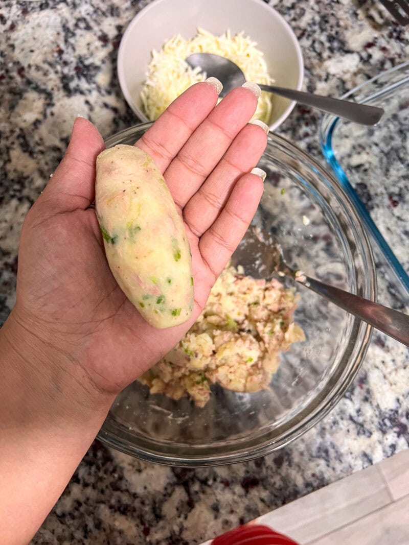 Hand shaping an oval croquette from tuna and potato mixture.