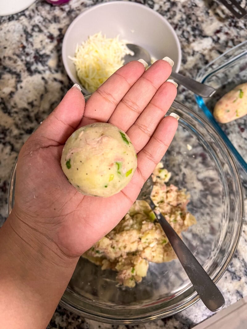 Hand shaping a round tuna and potato mixture into a ball.
