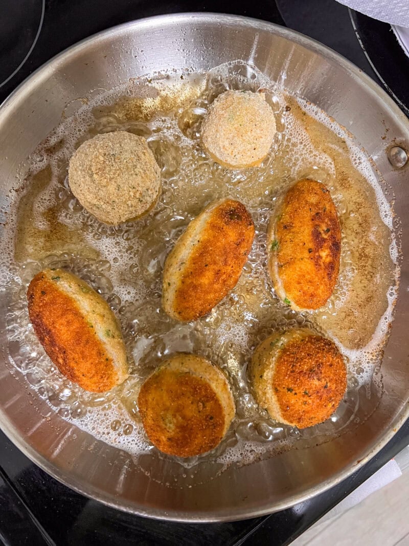 Tuna and potato croquettes frying in hot oil in a pan.