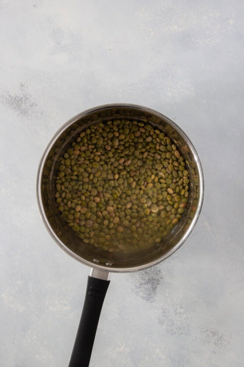 Green pigeon peas soaking in water in a stainless steel saucepan.